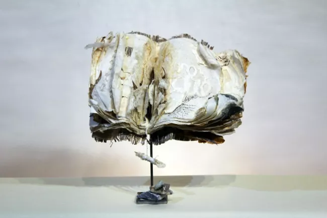 Sculpture en papier de Viviane Fontaine, intitulée ”Histoires secrètes”, représentant un livre ouvert, tenu en équilibre sur une tige de métal
